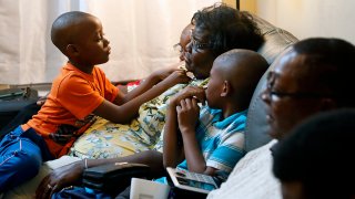 In this Nov. 25, 2019, file photo seven-year-old Jacolby Rhue, left, looks up at his adoptive mother, Linda Rhue, while sitting with family members in Newport News, Va. (Jonathon Gruenke/The Virginian-Pilot via AP)