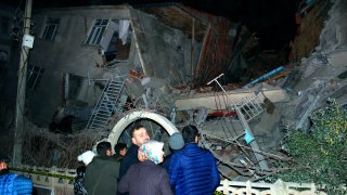 People look at a collapsed building after a 6.8 earthquake struck Elazig city center in eastern Turkey, Friday, Jan. 24, 2020.