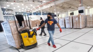 Workers unload pallets stacked with boxes of prepared meals that will be distributed to people in need, Thursday, April 30, 2020, at a temporary food distribution center at Basketball City on Pier 36 in New York.