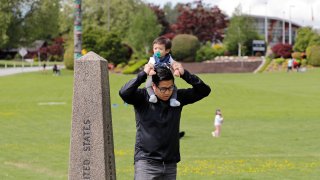 In this photo taken Sunday, May 17, 2020, Bryan Albano, walks with his son Zachary atop his shoulders in Canada at Peace Arch Provincial Park, adjacent to Peace Arch Historical State Park on the U.S. side, where people can walk freely between the two countries at an otherwise closed border, in Blaine, Wash.