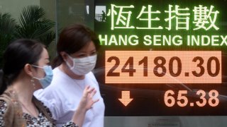 In this May 13, 2020, file photo, pedestrians wearing face masks walk past an electronic screen displaying the Hang Seng Index in Hong Kong, China.