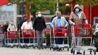People wearing protective masks queue up to go in a garden store in Munich, Germany, Monday, April 20, 2020.