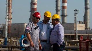 Employees stand near an Iranian national flag at the new Phase 3 facility at the Persian Gulf Star Co. (PGSPC) gas condensate refinery in Bandar Abbas, Iran