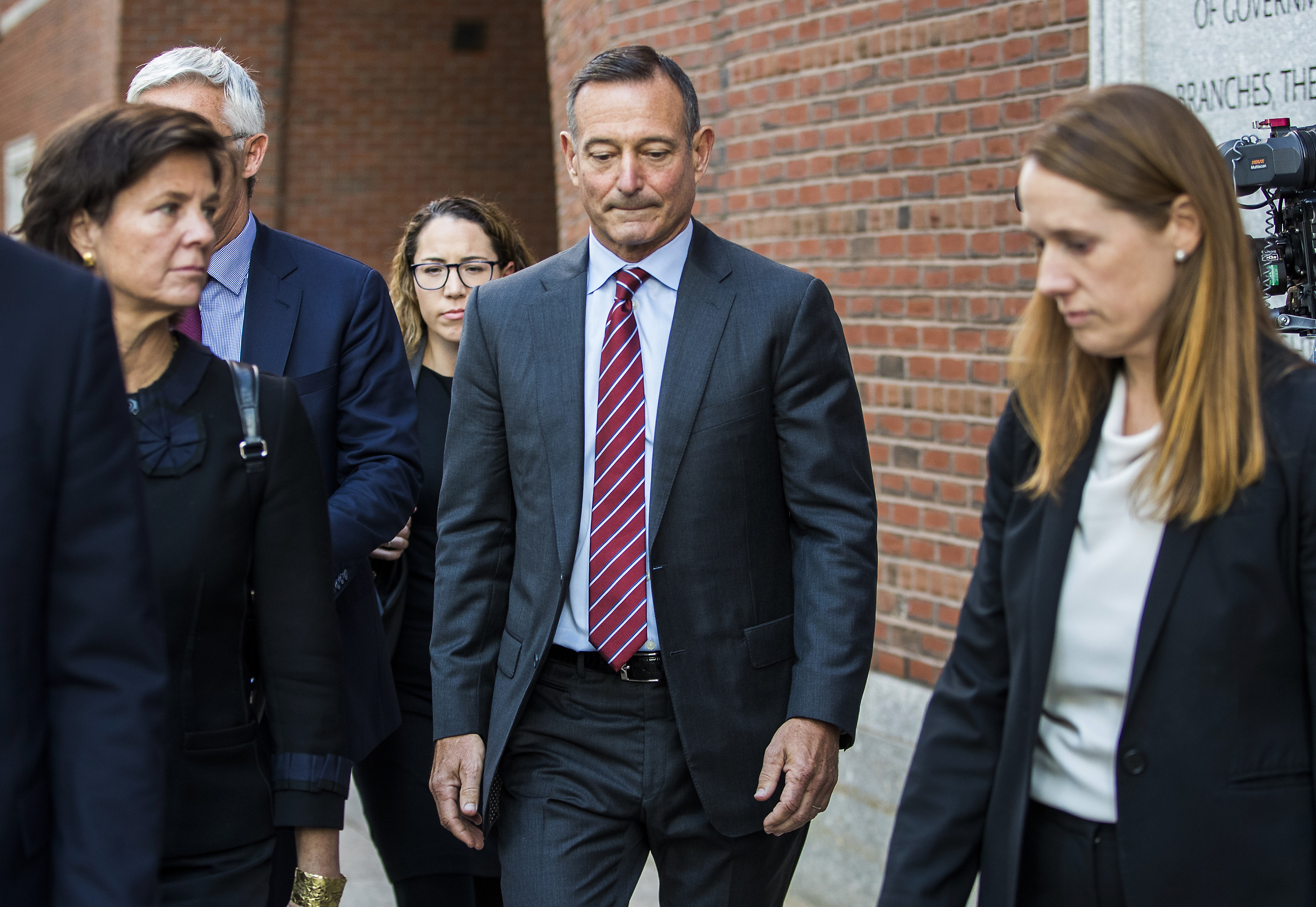In this Monday, Oct. 21, 2019, photo, Douglas Hodge, former chief executive office of Pacific Investment Management Co., center, exits federal court in Boston on Monday, Oct. 21, 2019. Hodge, accused of using a middleman to cheat his kids’ way into elite colleges, pleaded guilty to fraud and money-laundering conspiracy charges, the first in a flurry of plea changes as the government’s prosecution of the U.S. college admissions scam gathers steam.