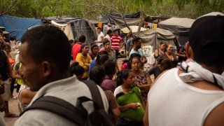 In this March 20, 2020, file photo, asylum seekers stand for a headcount at a makeshift migrant camp in Matamoros, Tamaulipas state, Mexico.