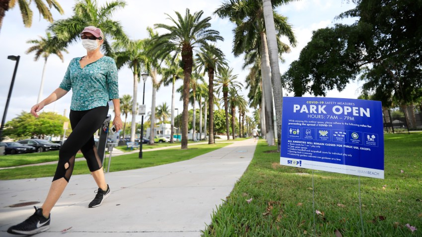 A woman wearing a face mask walks near a park in Miami Beach