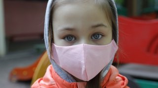 A girl in a face mask plays outside in a day care