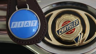 A Fiat logo on a keychain dangles next to the hood ornament of a Chrysler car