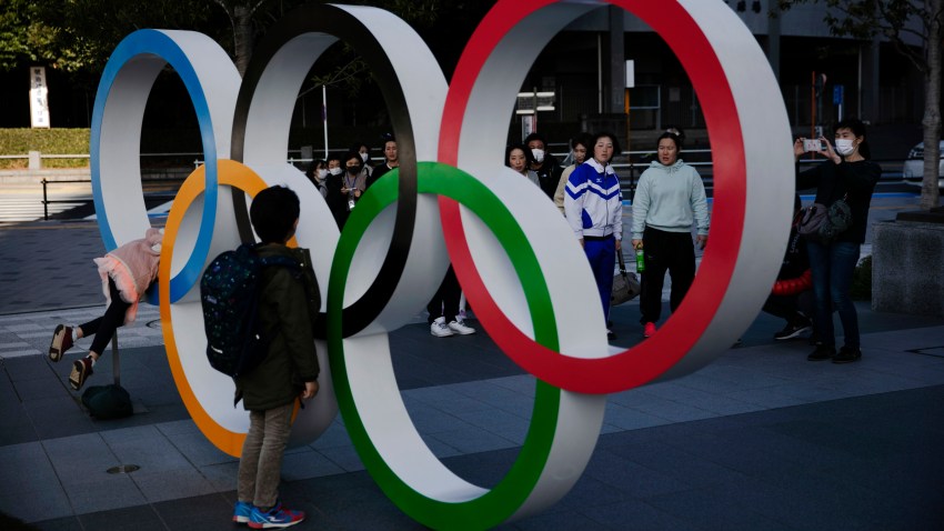 People wait in line to take pictures with the Olympic rings near the New National Stadium, Sunday, Feb. 23, 2020, in Tokyo.