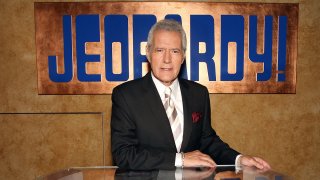 Alex Trebek poses with Jeopardy sign behind him