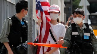A protester carrying an American flag as she is stopped by riot police during a protest outside the U.S. Consulate in Hong Kong, Saturday, July 4, 2020 to mark the American Independence Day or "the Fourth of July."