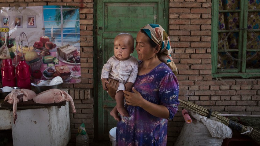 In this Sept. 12, 2016, file photo, a Uyghur woman holds a child in her home as they prepare food during the Corban Festival in Turpan County, in the far western Xinjiang province, China.