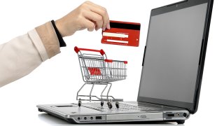 A laptop computer, a grocery cart and a hand holding a gift card.
