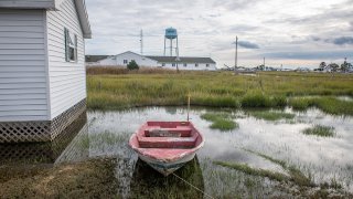 An empty rowboat sits atop the water-soaked ground alongside a house and a water tower stands in the distance in this undated photo from tiny Tangier Island, Virginia.