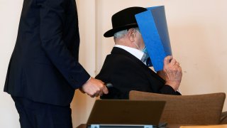 Bruno Dey, a former SS-watchman at the Stutthof concentration camp, hides his face behind a folder as he arrives on a wheelchair for a hearing in his trial on July 23, 2020 in Hamburg, northern Germany.