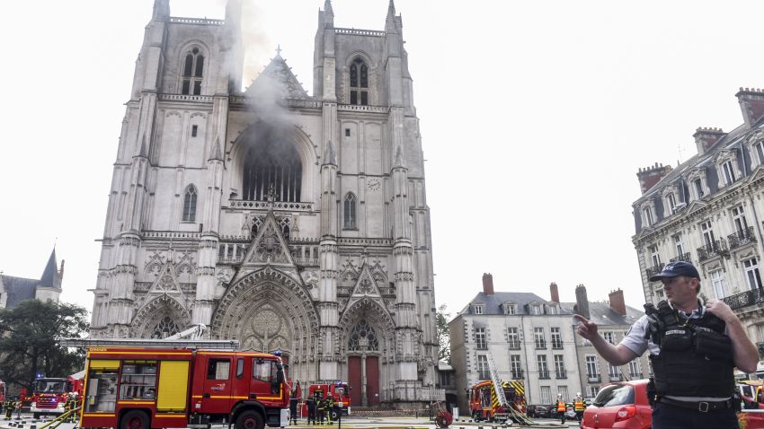 A French Police officer gestures as firefighters are at work to put out a fire at the Saint-Pierre-et-Saint-Paul cathedral in Nantes, western France, on July 18, 2020. - The major fire that broke out on July 18, 2020 inside the cathedral in the western French city of Nantes has now been contained, emergency services said. "It is a major fire," the emergency operations centre said, adding that crews were alerted just before 08:00 am (0600 GMT) and that 60 firefighters had been dispatched.