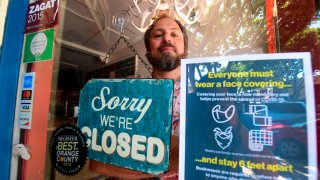 In this July 28, 2020, file photo, Gabriel Gordon stands behind the glass entrance door to his restaurant Beachwood BBQ, open for 14 years in Seal Beach, California, but closing soon due to the economic situation around the coronavirus pandemic.