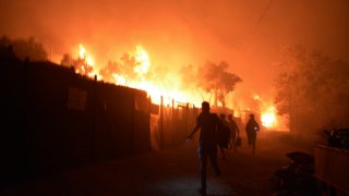 Refugees and migrants run as fire burns in the Moria refugee camp on the northeastern Aegean island of Lesbos, Greece, on Wednesday, Sept. 9, 2020. Fire Service officials say a large refugee camp on the Greek island of Lesbos has been partially evacuated despite a COVID-19 lockdown after fires broke out at multiple points around the site early Wednesday.