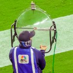 A man in an NBC Sports vest holds a large clear dish-shaped microphone