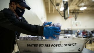 An election judge wearing a protective mask prepares mail-in ballots to be scanned
