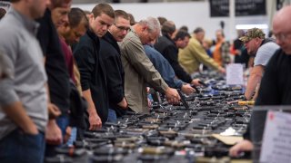 People look at handguns as thousands of customers and hundreds of dealers sell, show and buy guns and other items during The Nation's Gun Show at the Dulles Expo Center Oct. 3, 2015.