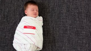 Sleeping swaddled infant with a "Hello my name is" sticker.