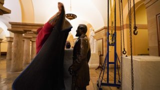 A worker is shown moments before covering a statue of Robert E. Lee with a cloth before it is removed from the U.S. Capitol. The statue had already been removed from its pedestal, which is shown empty surrounded by a pulley system.