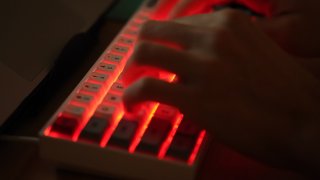 a young man types on an illuminated computer keyboard typically favored by computer coders