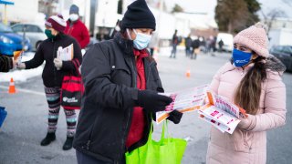 Community health workers with CASA de Maryland hand out brochures with coronavirus information to people lining up at a food distribution site behind Clifton Park Baptist Church in Silver Spring, MD. As vaccinations continue, local governments and commun