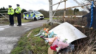 Flowers and messages of condolence for Sarah Everard are seen as police officers patrol near the woodland where police officers found human remains near Ashford, southeast England, on March 12, 2021, - A body found hidden in woodland in Kent has been identified as that of Sarah Everard. Metropolitan Police Assistant Commissioner Nick Ephgrave announced outside Scotland Yard on March 12, 2021, that the body found hidden in woodland in Kent has been identified as that of Sarah Everard.