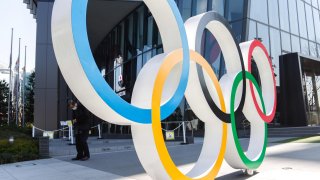 A man wearing a face mask stands behind the Olympic symbols of the five interlaced rings pictured near the National Stadium in Tokyo.