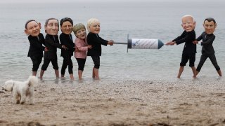 Activists wearing giant heads of the G7 leaders tussle over a COVID-19 vaccine syringe during an action by charity Oxfam to highlight intellectual property for vaccines on Swanpool beach in Falmouth, Cornwall on the sidelines of the G7 summit on June 11, 2021.