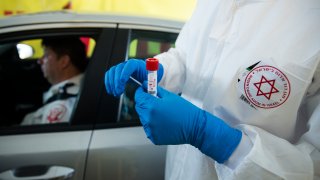 an Israeli medical worker holds a swab test for coronavirus at a drive-through site