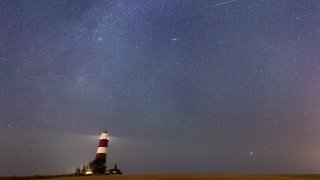 A meteor during the Perseid meteor shower seen over Happisburgh lighthouse, Norfolk, as the Earth flies through a cloud of cometary dust creating a spectacular display of celestial fireworks.