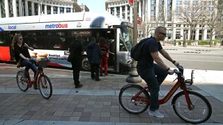 People board a Metrobus as two people riding Capital Bikeshare bikes ride past