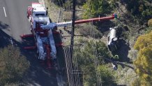 Workers move a car after a rollover accident involving golfer Tiger Woods, Feb. 23, 2021, in Rancho Palos Verdes, California. Woods suffered leg injuries in the one-car accident and was undergoing surgery, authorities and his manager said.