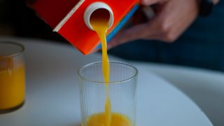 Orange juice is poured into a glass from a carton of juice.