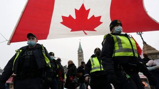 Police officers walk past a giant Canadian flag in front of Parliament as demonstrators continue to protest the vaccine mandates on Feb. 11, 2022, in Ottawa, Canada.