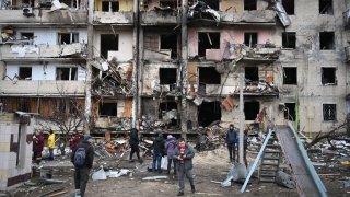 People gather in front of a damaged residential building at Koshytsa Street, a suburb of Kyiv, where a military shell allegedly hit, Feb. 25, 2022. Russian forces reached the outskirts of Kyiv on Friday as Ukrainian President Volodymyr Zelensky said the invading troops were targeting civilians and explosions could be heard in the besieged capital. Pre-dawn blasts in Kyiv set off a second day of violence after Russian President Vladimir Putin defied Western warnings to unleash a full-scale ground invasion and air assault on Thursday that quickly claimed dozens of lives and displaced at least 100,000 people.