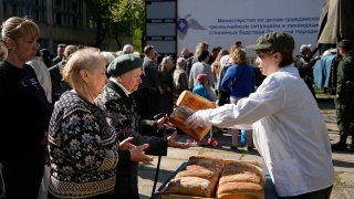 Local civilians gather to get humanitarian aid, bread and water distributed by Donetsk People Republic Emergency Situations Ministry in Mariupol, in territory under the government of the Donetsk People's Republic, eastern Ukraine, Friday, April 29, 2022. This photo was taken during a trip organized by the Russian Ministry of Defense.