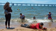 A man lies on the beach as his family plays in the Chesapeake Bay trying to escape the heat at Sandy Point State Park in Annapolis, Maryland on June 29, 2021. - The scorching heat -- which is breaking records in Canada and the United States dating back more than 80 years -- has been blamed on a high-pressure ridge trapping warm air in the region. (Photo by JIM WATSON / AFP) (Photo by JIM WATSON/AFP via Getty Images)