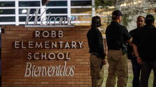 Law enforcement officers speak together outside of Robb Elementary School