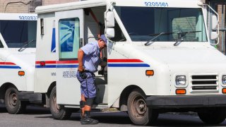 A United States Postal Service (USPS) worker exits a Grumman Long Life Vehicle.