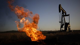 A photo of a natural gas flare burning near an oil pump jack at the New Harmony Oil Field in the U.S. on June 19, 2022.