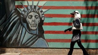 An Iranian woman walks by a mural painting on the wall of the former US embassy in the Iranian capital Tehran on August 7, 2018.