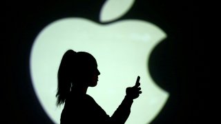 Silhouette of a mobile user seen next to a screen projection of the Apple logo in this picture illustration taken March 28, 2018.