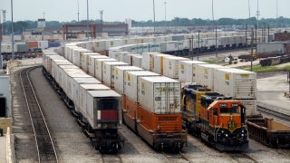 Shipping containers sit at a railway facility waiting to be transferred.