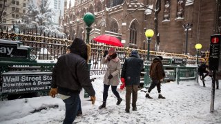 Pedestrians walk in snow past the Wall Street subway station near the New York Stock Exchange.