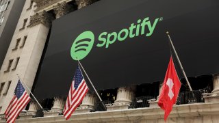 The Spotify logo hangs on the facade of the New York Stock Exchange with U.S. and a Swiss flag as the company lists its stock with a direct listing in New York, April 3, 2018.