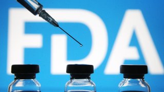 Vials and a medical syringe seen displayed in front of the Food and Drug Administration (FDA) of the United States logo. FDA finds the COVID-19 vaccine.